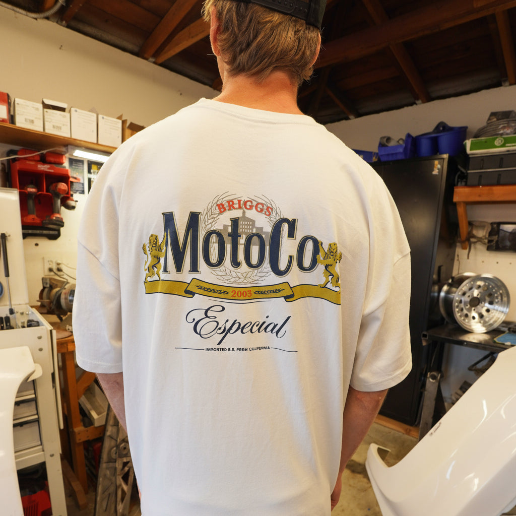 Dayton Briggs wearing a cream colored t-shirt with ' Briggs MotoCo' branding like the classic Modelo logo in a workshop setting
