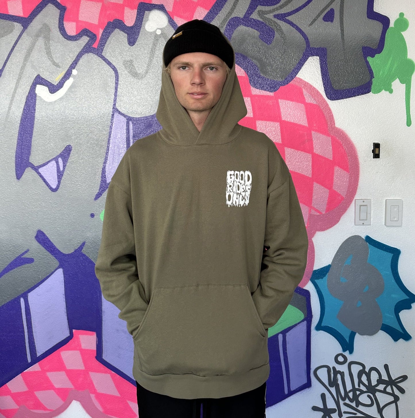 Dayton is wearing the Good Rides Only Olive Green Motocross Sweatshirt standing against a graffiti Wall