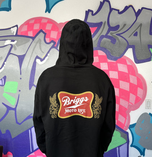 Dayton wearing a black hoodie with 'Briggs Moto Life' logo, spoofing the old school Miller High life logo on the back, standing in front of a colorful graffiti wall.