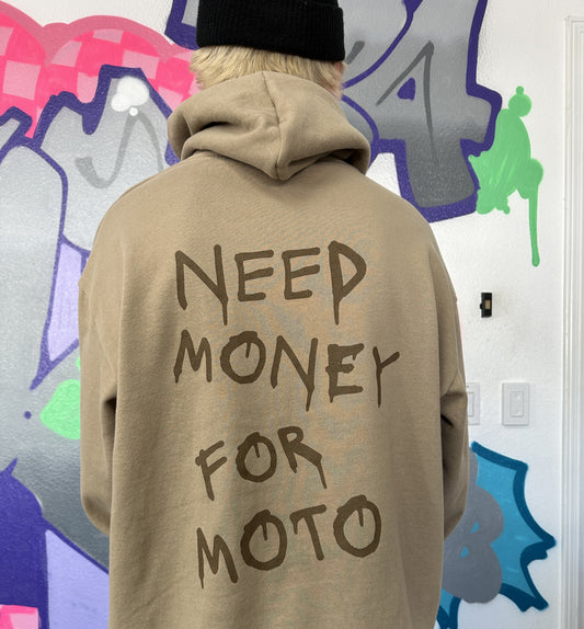 Dayton is wearing a tan hoodie with brown text 'NEED MONEY FOR MOTO' printed in a spray-paint like font on the back, standing in front of a colorful graffiti wall.